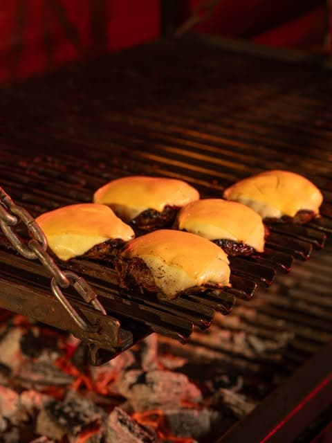 Hamburguesas con queso cheddar derretido sobre la parrilla con brasas
