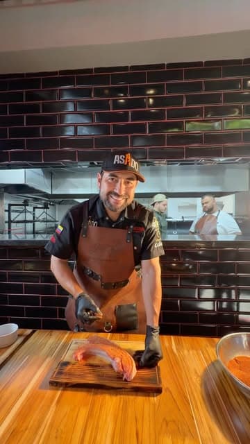 Chef trabajando un salmón sobre tabla de madera en cocina de ladrillo