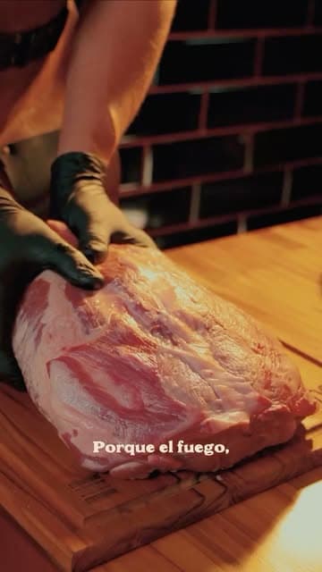 Manos enguantadas trabajando un brisket crudo sobre una tabla
