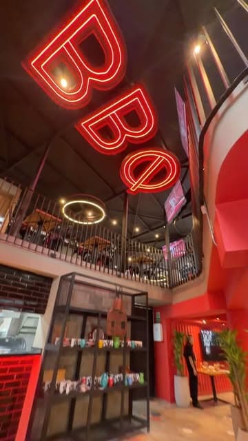 Interior del local con neón rojo de BBQ, mezzanine y escalera de caracol roja sobre pared de ladrillo